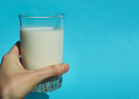 A glass of milk in hand on a blue background with copy spaceの写真素材