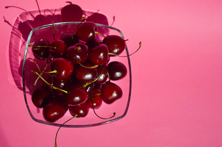 Cherries in a glass vase on a pink background.の写真素材