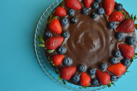 Chocolate cake with strawberries and blueberries on a blue background.