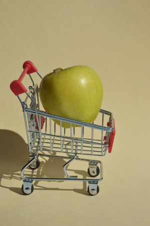 Green apple in a shopping cart on a beige background with a shadow