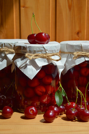 Cherry jam in a glass jar and ripe cherries on a wooden backgroundの写真素材
