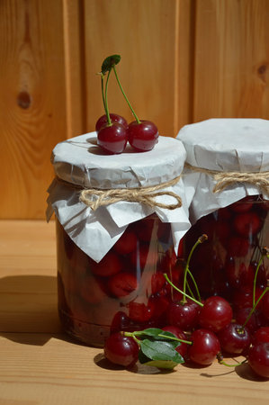 Cherry jam in a glass jar and fresh cherries on a wooden backgroundの写真素材
