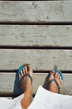 Female feet in blue flip flops on a wooden deck on a sunny day