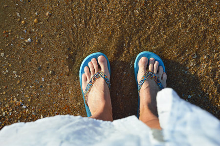 Female feet in blue slippers on the beach. View from above.