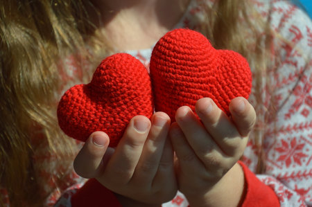 Two red knitted hearts in the hands of a girl on a blue backgroundの写真素材