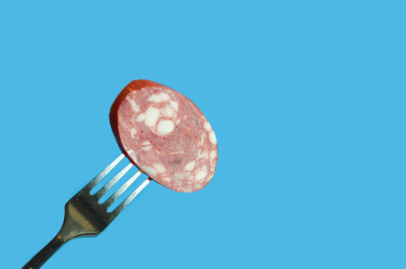 Slices of salami on a fork on a blue backgroundの写真素材