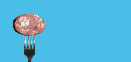 Slice of salami on a fork on a blue background.の写真素材