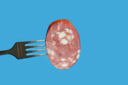 Slices of salami on a fork on a blue backgroundの写真素材