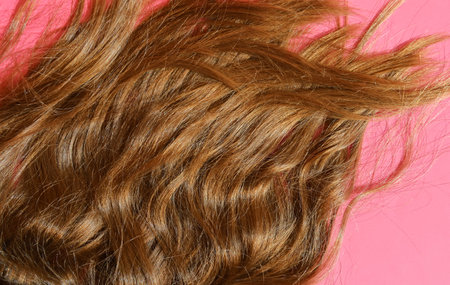 Curly brown hair on pink background. Top view. Copy space.
