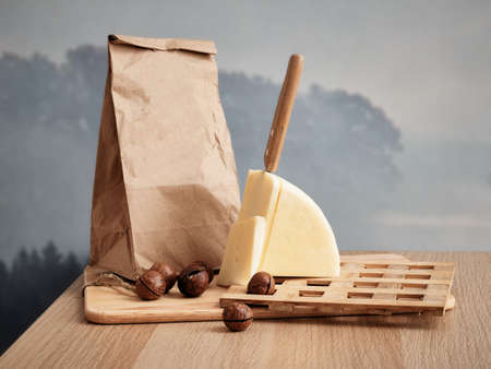 Delivery package with caciotta cheese near Paper bag. A sliced piece with knife on a wooden standの写真素材