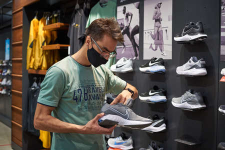 Nizniy Novgorod / Russia - 15 07 2020: Young Man in medical face mask chooses sneakers in shopping store. New reality after covid 19 outbreak.のeditorial素材