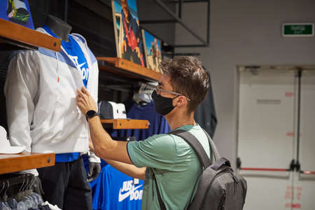 Nizniy Novgorod / Russia - 15 07 2020: Young caucasian man in a medical black mask chooses clothes in the supermarket. The concept of social distance and protectionのeditorial素材