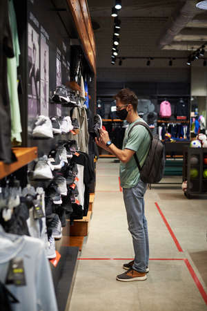 Nizniy Novgorod / Russia - 15 07 2020: Young Man chooses sneakers in shopping store wearing medical face mask. The concept of social distanceのeditorial素材