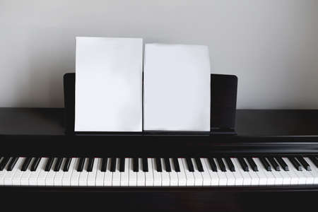 Empty piano with empty sheet of paper in front of white wall with a black wall lamp