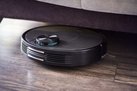 Top view of Robot vacuum cleaner on wooden floor cleaning under the bed, Smart robotic automation wireless cleaning technology machine in living roomの写真素材
