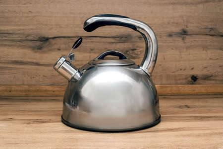 Stainless steel whistling kettle on the wooden surface, wooden background