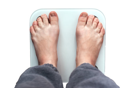 Top View of a person with bare feet standing on a digital white scale, against white backgroundの写真素材