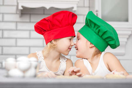 Two cheerful girls cook in colored caps prepare doughの写真素材