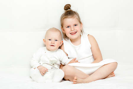 Two pretty little sisters in white T-shirts in bedの写真素材