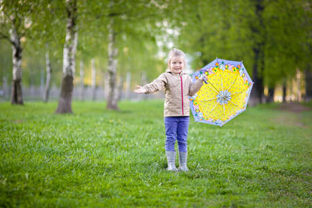 happy girl 5 years under a yellow umbrella walks on the green grass after the rainの写真素材