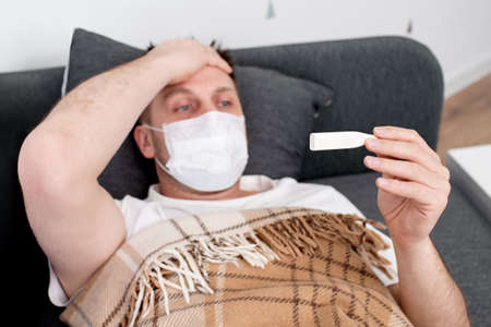 sick man lies under a blanket with a tablet. near a glass of water and pillsの写真素材