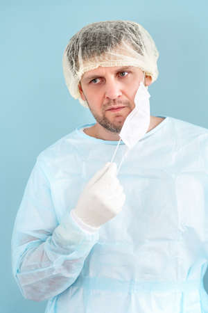 Portrait shot of the Caucasian tired man doctor in medical hat taking off mask from his mouth