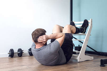 Strong Athletic Fit Man in T-shirt and Shorts is Doing Abdominal Crunch Workout at Home in His...