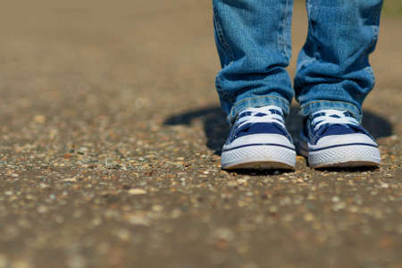 Childrens legs in denim sneakers are hanging on the background of the pavement.の写真素材