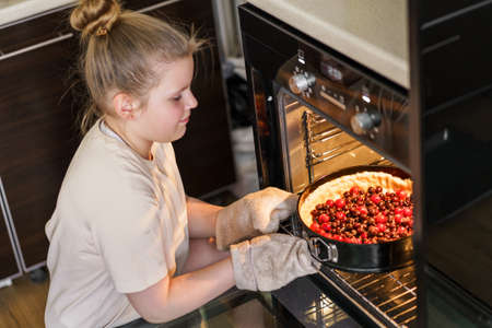 Happy little daughter take on pie from oven cooking dessert at home, smiling small girl child feel excited baking cookies in modern kitchenの写真素材