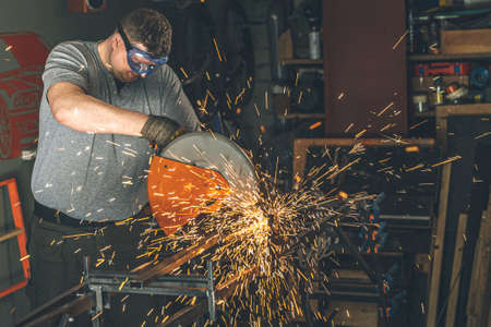 Professional mechanic man is cutting steel metal with rotating carbon blade cutter. Steel industry...