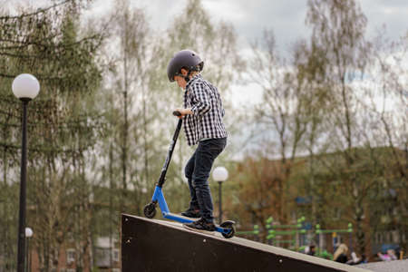 A boy on a scooter and in protective helmet do incredible stunts in skate park. Extreme jump. The...