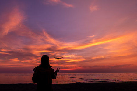 A man on the beach catches a drone in the sunset light.の写真素材