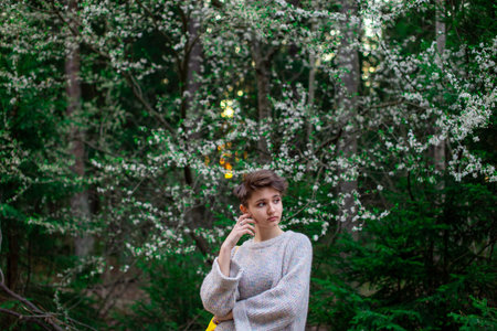 Portrait of a teenage girl in nature. Short dark hair. A large tree with green foliage and small white flowers.の写真素材