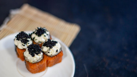 Sushi in a white plate on a blue marble table. There is a bamboo mat nearby. Sushi with red fish, cottage cheese and caviar. Banner sushi.の写真素材