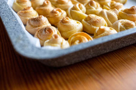 Fresh pastries in a metal baking tray. The corner of the baking tray in small buns, baking in the shape of a rose. Wooden table.の写真素材