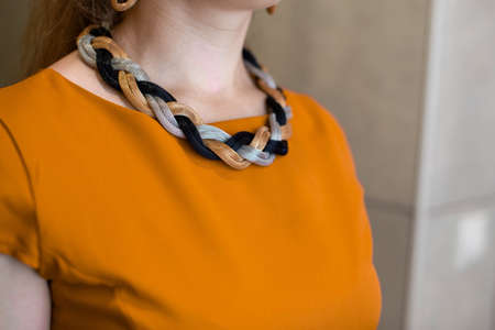 Decoration on neck of a woman. Massive braided decoration in gold, silver and black colors. Orange dress. A woman neck. Without a face.の写真素材