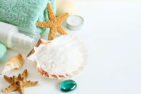 Spa cosmetics and towel with sea stars and salt in the scallop shell on a white background on top
