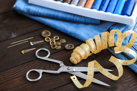 tools and materials for sewing thread needles buttons lie on a dark wooden background, the work of a...