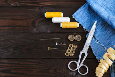tools and materials for sewing thread needles buttons lie on a dark wooden background, the work of a...