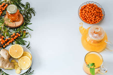 Hot sea buckthorn tea with lemon, ginger and honey on a white table top view. Twigs and berries of...