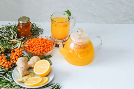 Hot sea buckthorn tea with lemon, ginger and honey on a white table