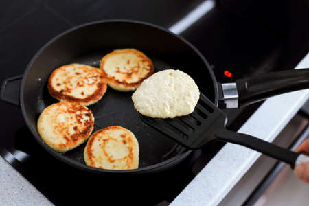 pancake on a spatula over a frying pan, cheesecakes on a hot pan, breakfast preparation
