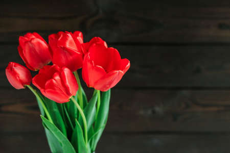 Composition with red tulips on a dark wooden background for March 8. greeting card with space for textの写真素材