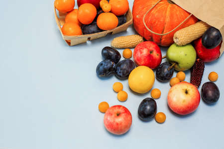 Package with scattered colored fruit on a blue background. Plums, tangerines, lemon, apples, pumpkin. Shopping in the store. the view from the topの写真素材