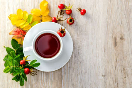 Tea with fresh rosehip berries on a wooden surface with space for text.