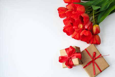 a beautiful bouquet of red tulips lies on a white surface next to the gift boxesの写真素材