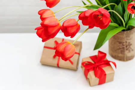 bouquet of red tulips in a vase on the table with giftsの写真素材