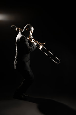 Trombone player. Trombonist playing jazz musician. Man playing trumpet brass instrument isolated on black full length profile portraitの写真素材