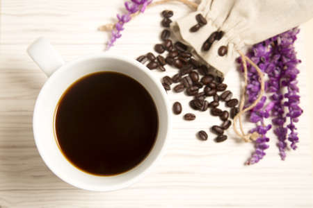 Cup of coffee and coffee beans in a fabric bag on the wood background