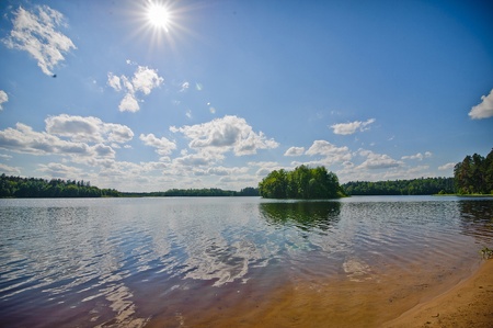 Beautiful landscape of the lake. The dark blue sky with clouds, the sun, yellow sand and an islet in the distance.の写真素材